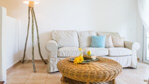 Ein Wohnzimmer mit einem weißen Sofa, einem runden Korbtisch und einer Stehlampe mit weißem Lampenschirm.