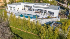 Una casa moderna de dos pisos con una amplia piscina, mobiliario de exterior y un jardín bien cuidado.