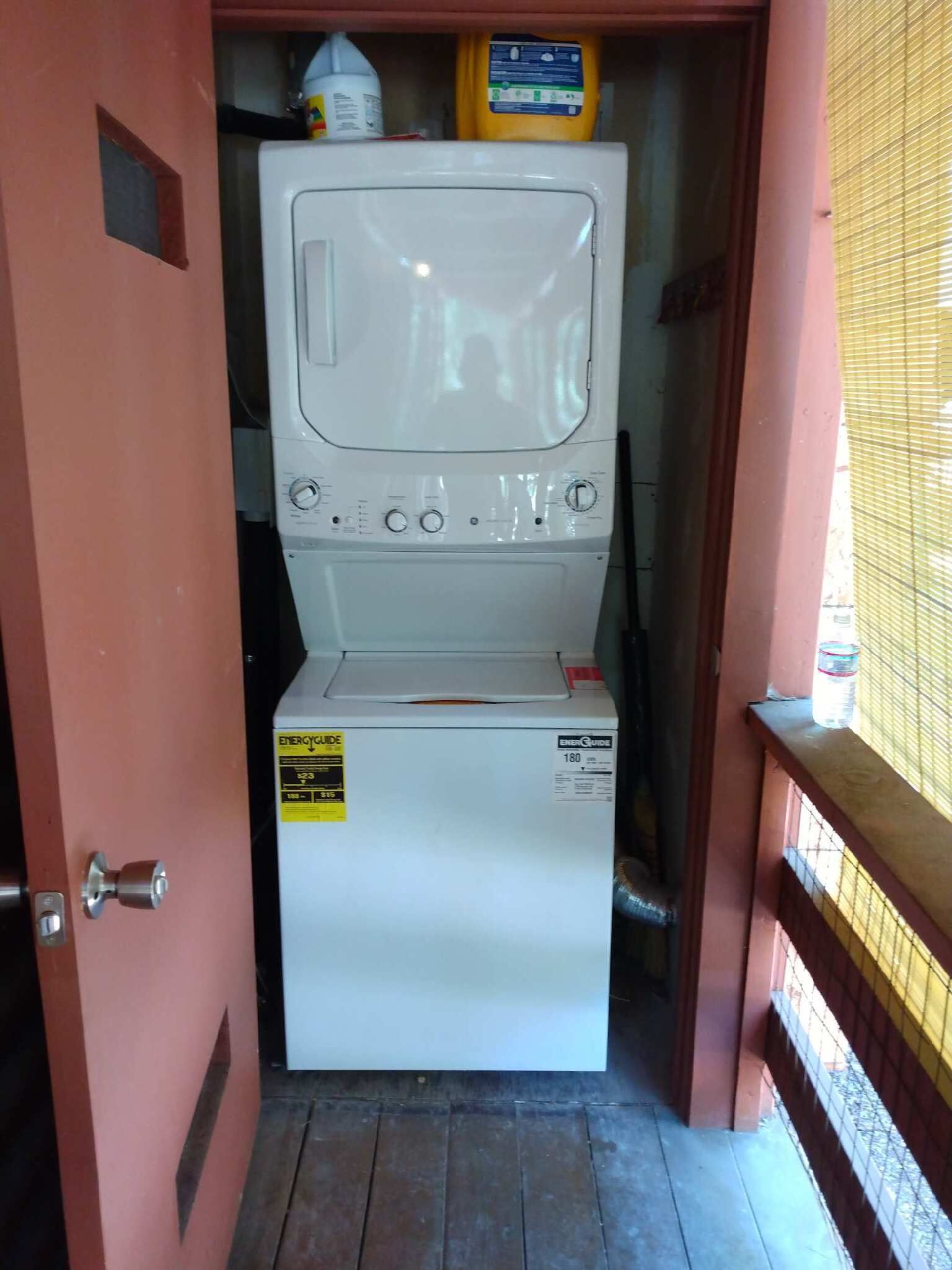 Máquina de lavar compacta e branca num espaço pequeno, com uma porta de um lado e uma janela do outro.