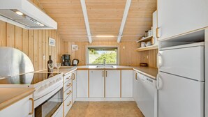 Une cuisine moderne avec un lambris en bois, des armoires blanches, une hotte de cuisinière en acier inoxydable et une fenêtre donnant sur la verdure à l’extérieur.