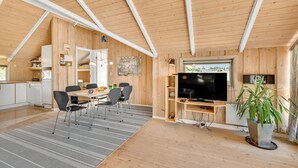 Une pièce chaleureuse et bien éclairée, avec un plafond en bois, un coin repas comprenant une table et des chaises, un téléviseur et une plante en pot.