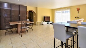 A modern living room with a dining area, featuring a TV, a sofa, and a large window with curtains. - Amazing home in Mornas (Mornas)