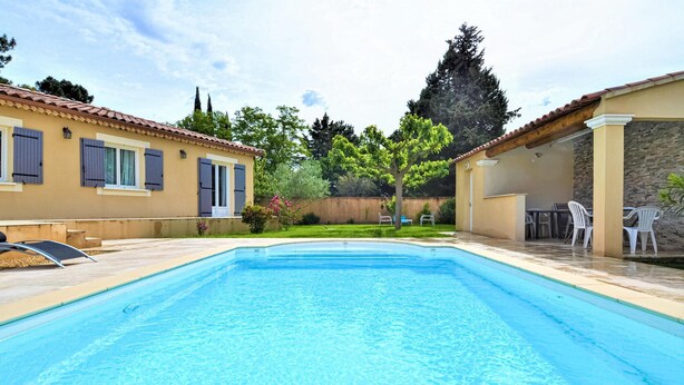 Una piscina rectangular con solárium empedrado, rodeada por un porche cubierto con mobiliario exterior.