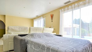 A bedroom with a bed, two white chairs, a large window with curtains, and a view of a pool. - Amazing home in Mornas (Mornas)