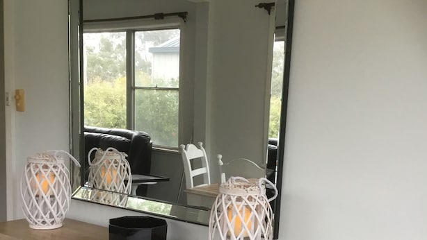 Una habitación con un espejo grande, un tocador de madera con cajones y dos faroles blancos sobre el tocador.