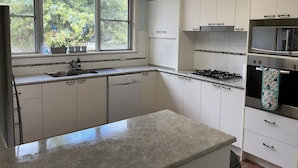 Una cocina con armarios blancos, estufa a gas, microondas y ventana con plantas.