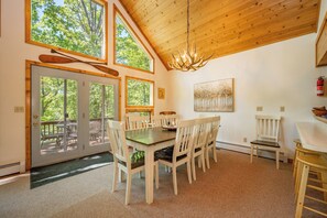 A dining area with a wooden ceiling, large windows, and a chandelier.
