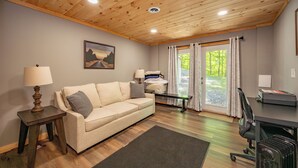 A room with a wooden ceiling, a sofa, a desk, a lamp, a chair, and a window with curtains. - Dockside Dog Friendly Retreat w/ Views & Arcades (Swanton)