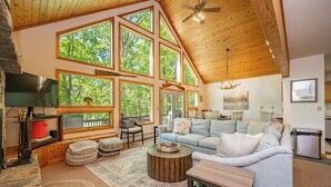 A spacious living room with a high ceiling, large windows, a fireplace, and a cozy seating area. - Dockside Dog Friendly Retreat w/ Views & Arcades (Swanton)