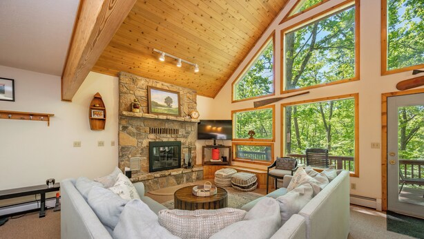 A cozy living room with a stone fireplace, large windows, and a high ceiling. - Dockside Dog Friendly Retreat w/ Views & Arcades (Swanton)