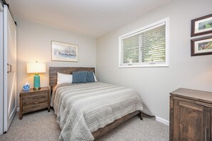 A bedroom with a bed, nightstand, lamp, and a window with blinds.