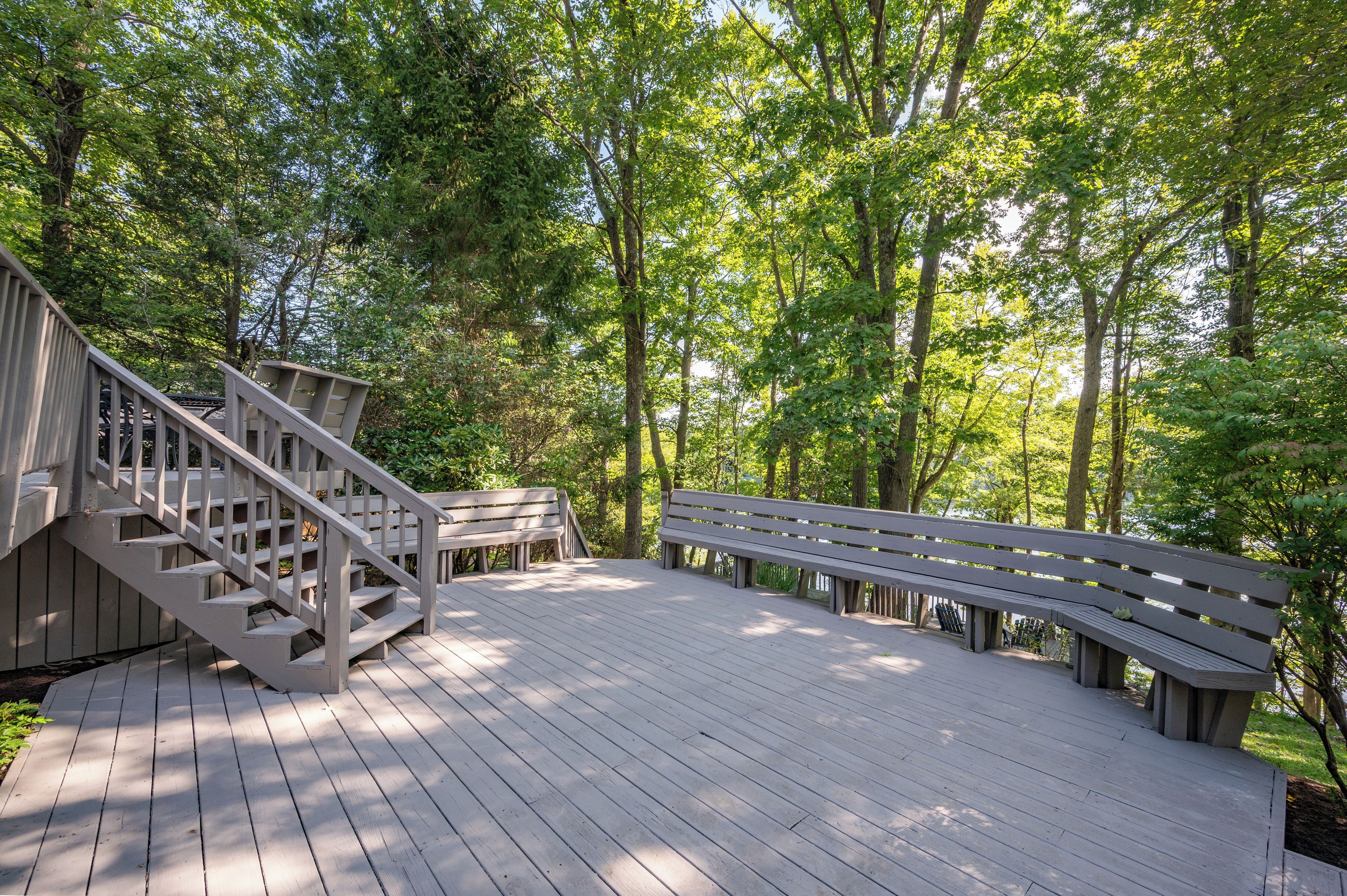 Une terrasse en bois avec un escalier menant à une zone abritée, le tout entouré d’arbres.