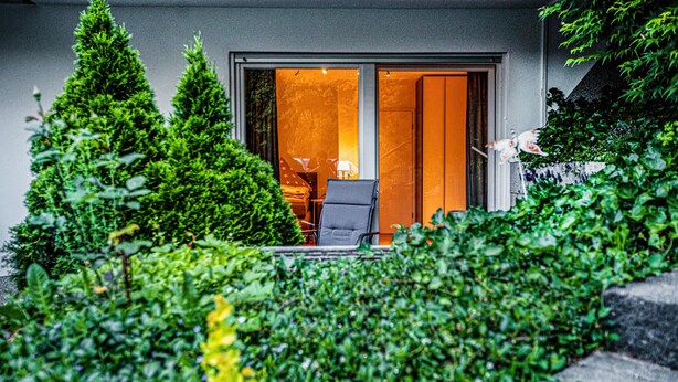Un bâtiment moderne avec une porte en verre donnant sur une pièce qui contient un lit et une lampe.