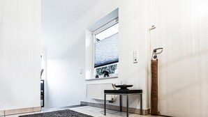 Un couloir avec une fenêtre, un radiateur, une table et une porte.