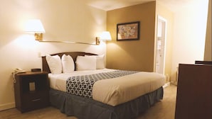 Una cama bien tendida con una colcha estampada, dos lámparas de noche, una mesita de noche con un teléfono y un cuadro enmarcado en la pared.