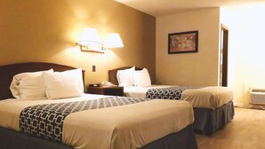 Ein Hotelzimmer mit zwei Betten, jedes mit einem gemusterten Überwurf und Kissen. Über den Betten befinden sich Wandleuchten und an der Wand hängt ein gerahmtes Bild.