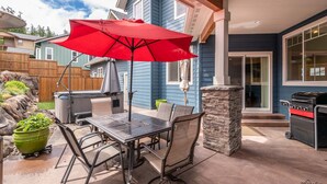 Un patio exterior con una mesa, sillas, una sombrilla roja, un jacuzzi y una parrilla.