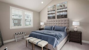 Un dormitorio con una cama grande, dos mesitas de noche, un banco, un radiador y una obra de arte en la pared.