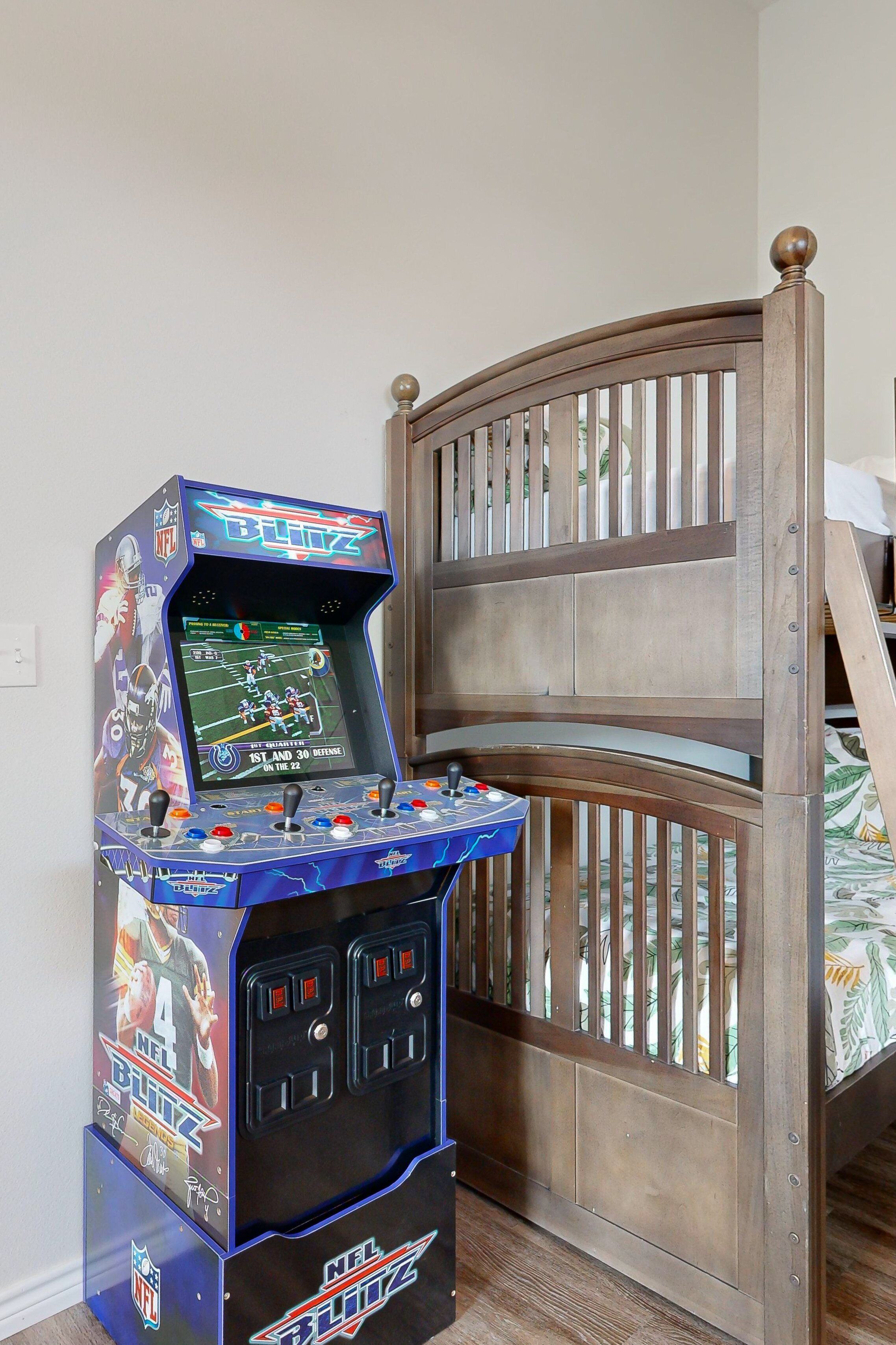 A video game arcade machine labeled "NFL Blitz" next to a wooden bed frame.