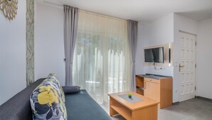 Moderni olohuone, jossa on sohva, pieni puinen pöytä, seinälle asennettu televisio ja koodilukolla varustettu ovi.