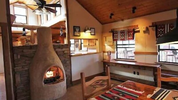 Um interior acolhedor com lareira de pedra, teto de madeira e uma área de refeições com mesa e cadeiras.