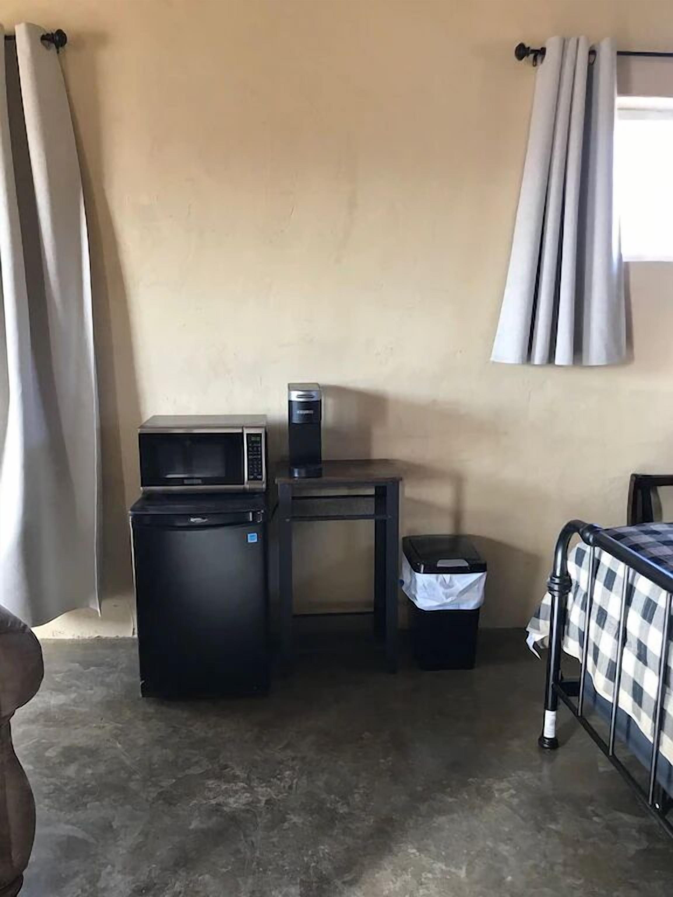 Ett kompakt hotellrum med ett litet pentry, ett litet bord, en papperskorg och en säng med ett rutigt överkast.