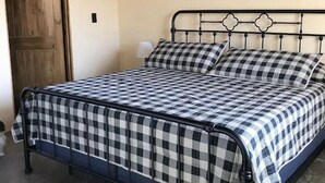 Uma cama de solteiro com estrutura de metal e colcha xadrez.