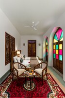 A traditional room with a sofa, chairs, a table with fruits, and colorful stained glass windows.