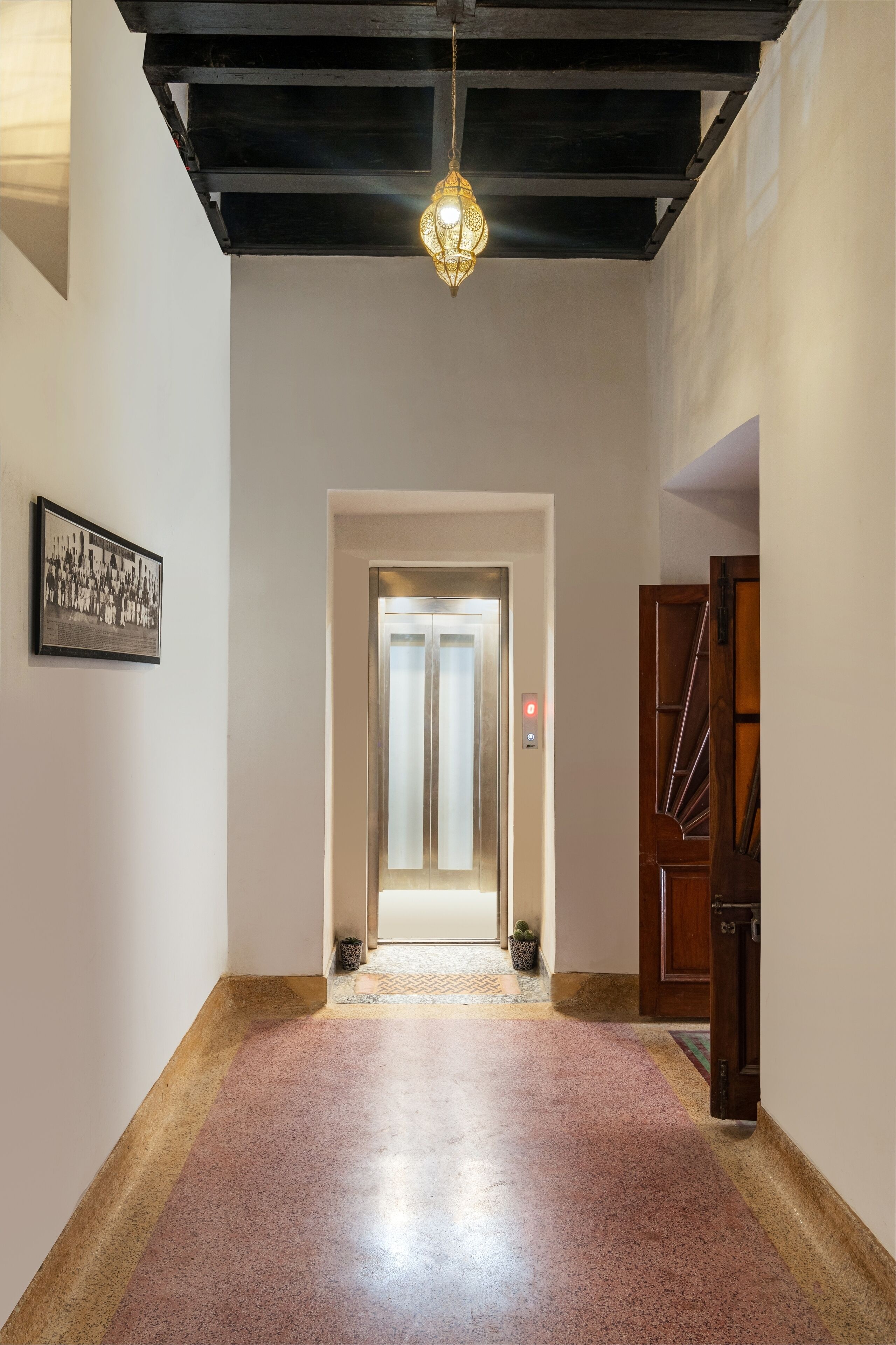 Un couloir doté d’un plancher poli, d’un luminaire suspendu, d’une photographie encadrée accrochée au mur et d’une porte ornée d’un panneau décoratif.