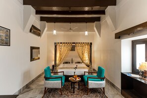 A hotel room with a bed, two chairs, a small table with fruit, a lamp, and a window. - WelcomHeritage Badi Kothi  (Prayagraj)