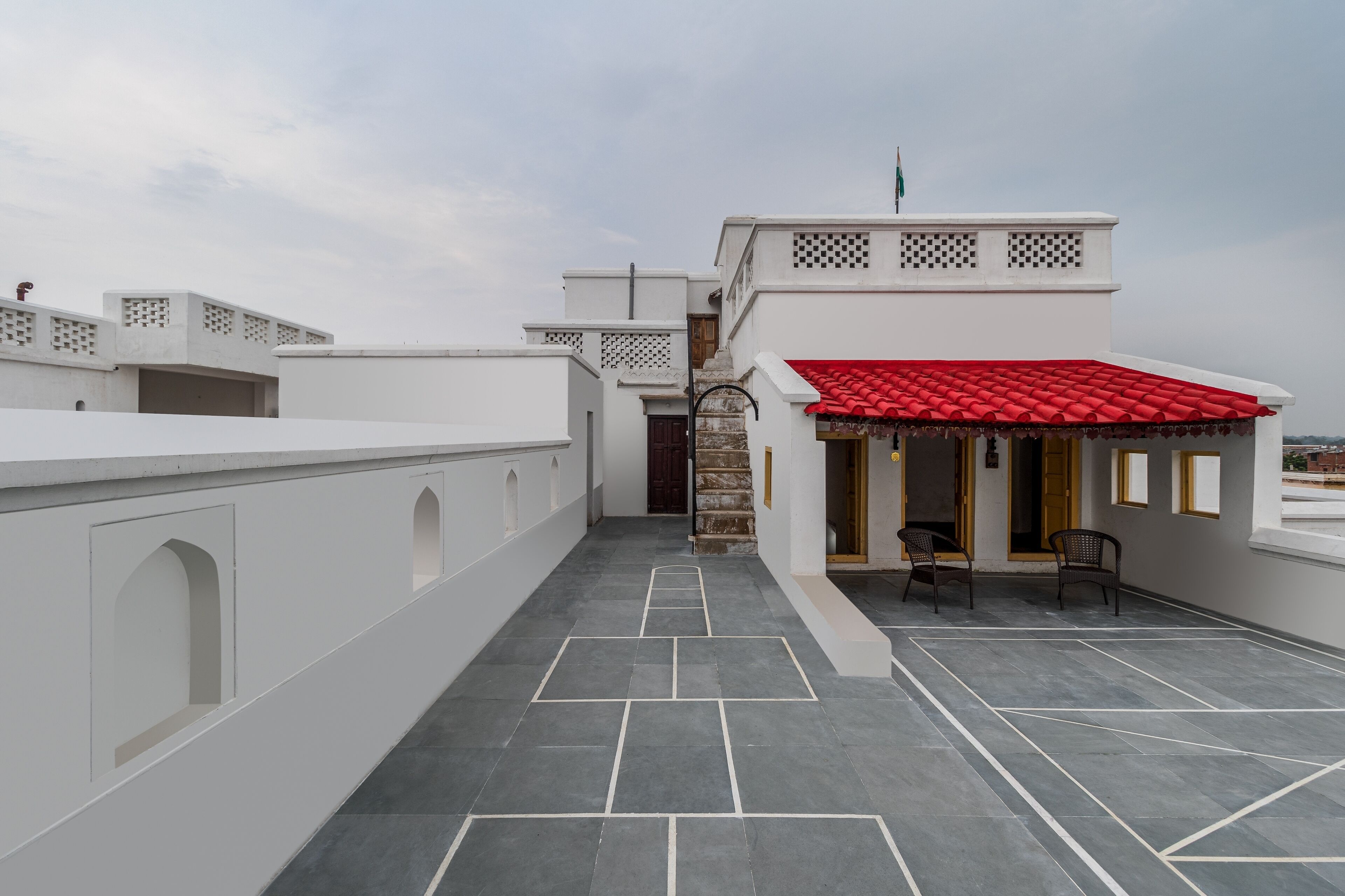 Una terrazza sul tetto con un tetto in tegole rosse, una scala che conduce a un livello superiore e un’area salotto con sedie.