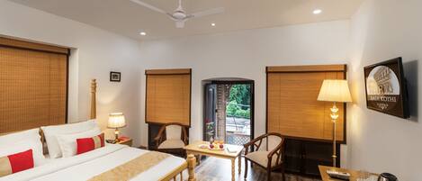 A hotel room with a bed, a desk, chairs, a ceiling fan, and a view of the outside.