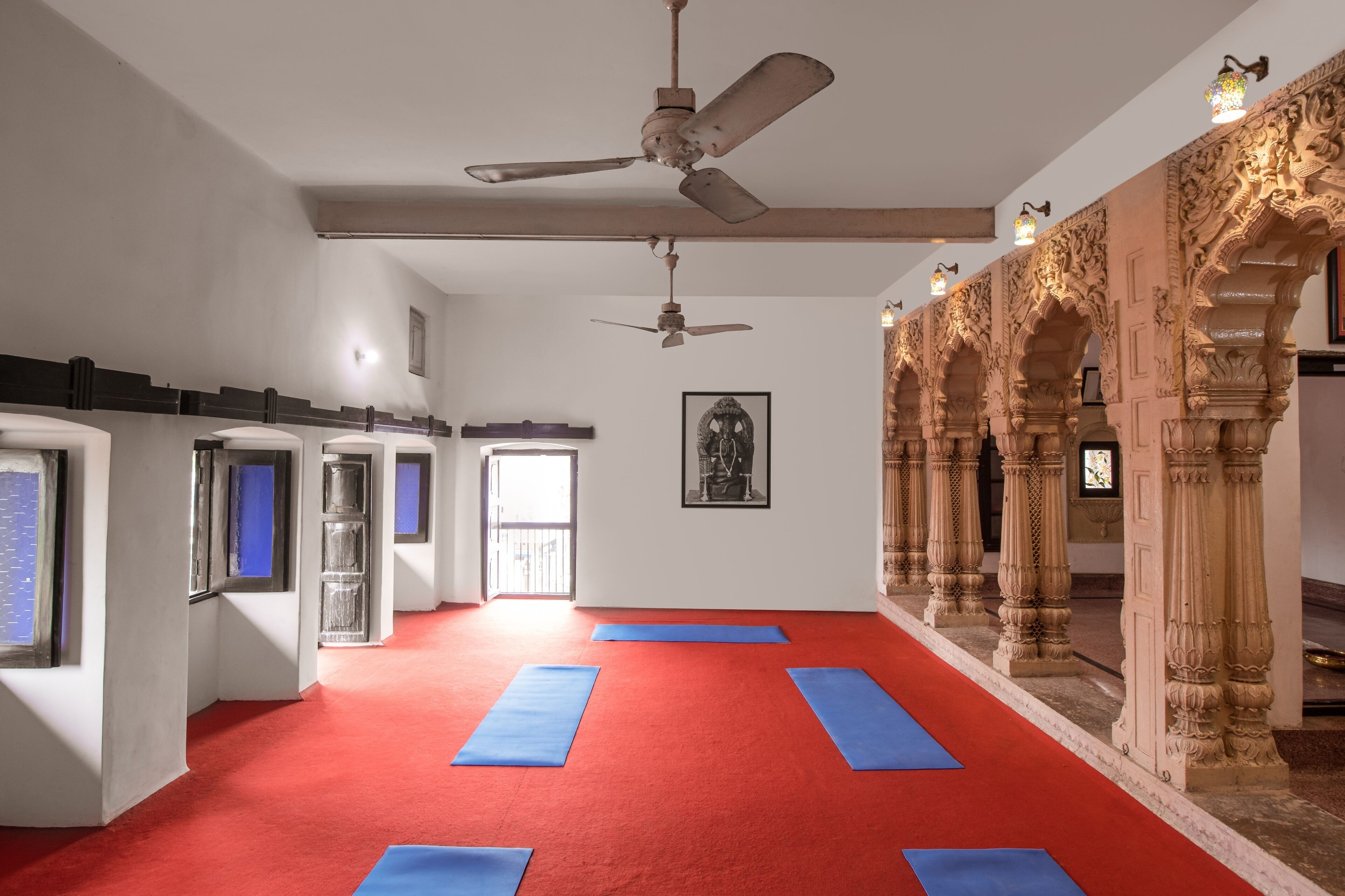 Un studio de yoga avec des tapis rouges, des ventilateurs de plafond et des colonnes richement décorées.