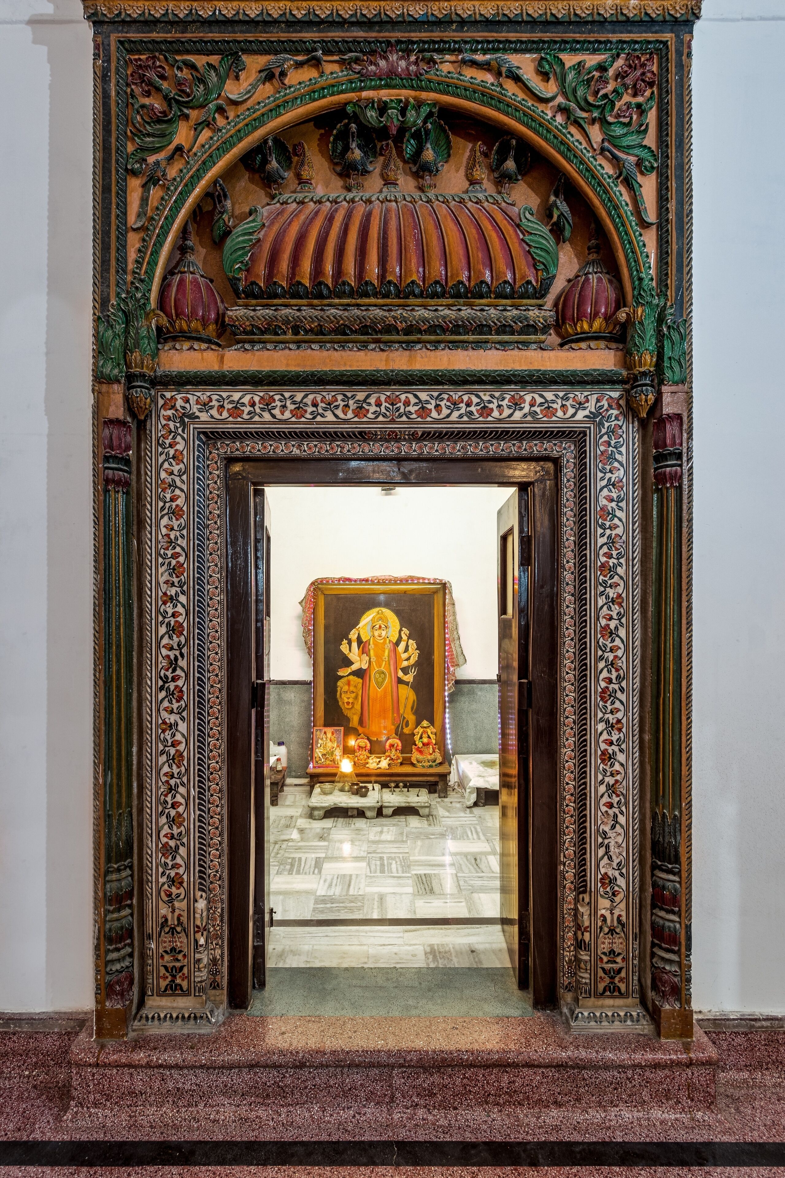 Un portail richement décoré, orné de sculptures complexes, et une peinture encadrée représentant une divinité.