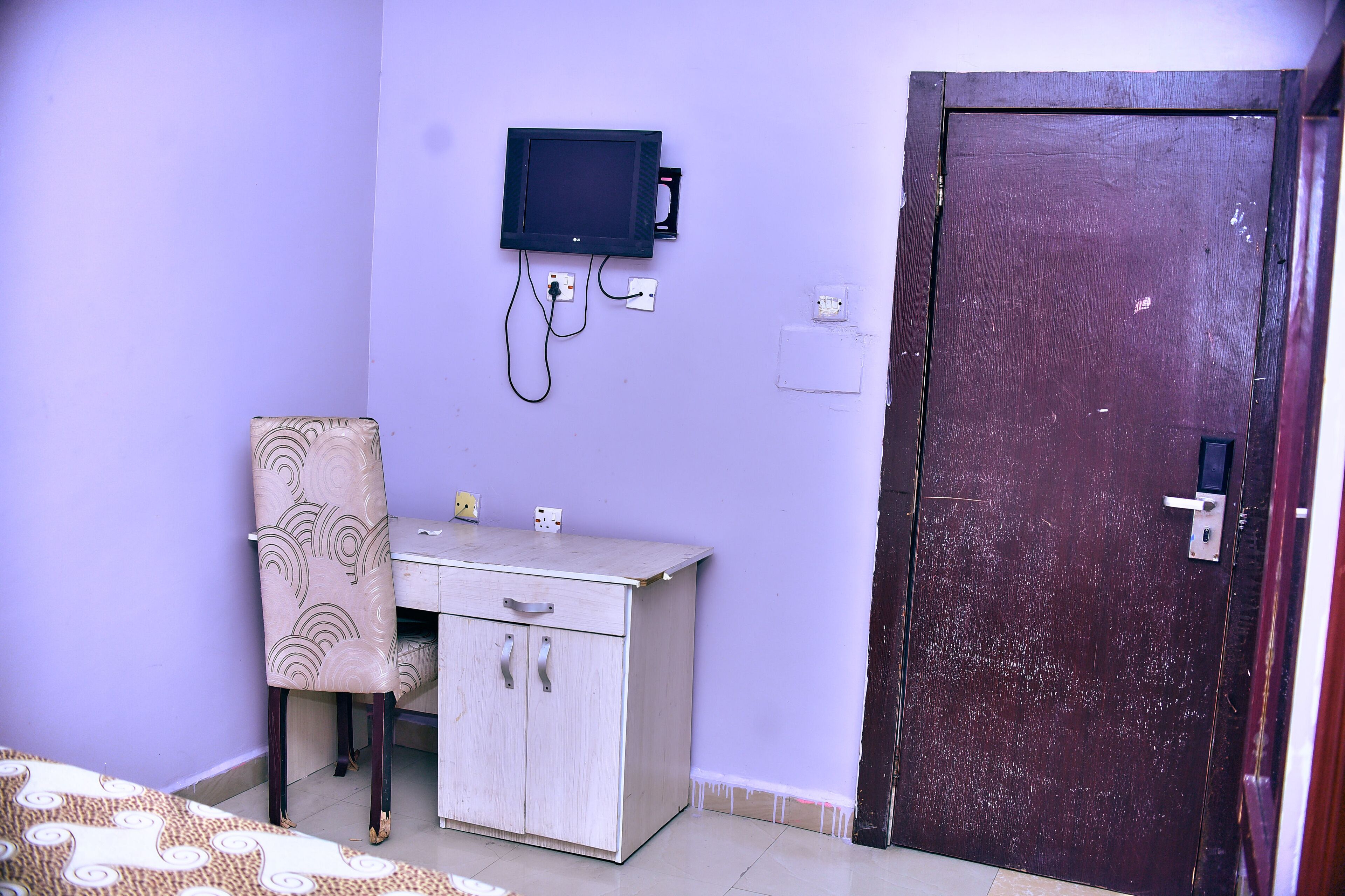 Quarto com escrivaninha, cadeira e televisão fixada na parede.