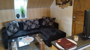 A living room with a black sectional sofa, a glass coffee table, and a wooden door. - Ferienwohnung "Am Vulkanpfad" (Ettringen)