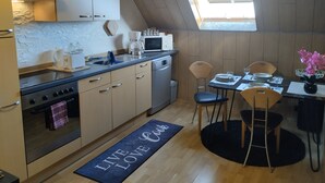 A compact kitchen with a dining area, featuring a built-in oven, microwave, and a small dining table with chairs. - Ferienwohnung "Am Vulkanpfad" (Ettringen)