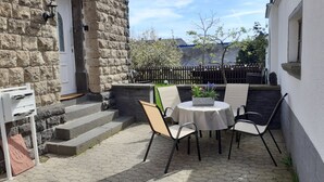 A patio with a table and chairs, a stone wall, and a wooden fence. - Ferienwohnung "Am Vulkanpfad" (Ettringen)
