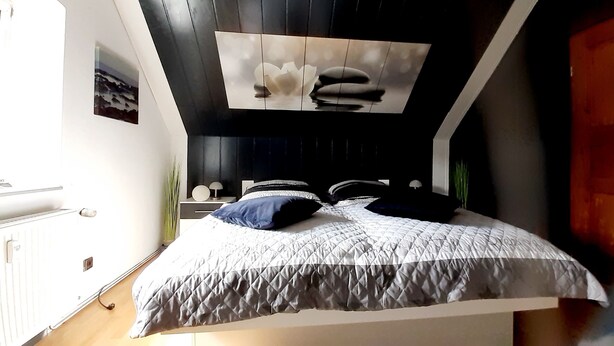 A modern bedroom with a bed, a nightstand, and a wall-mounted artwork. - Ferienwohnung "Am Vulkanpfad" (Ettringen)