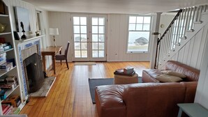 A spacious living room with a brown leather sofa, a fireplace, and a view of the sea through large windows. - Rare! Private Beachfront House in Madison CT - Sleeps 8 - Last Min Availability (Madison)
