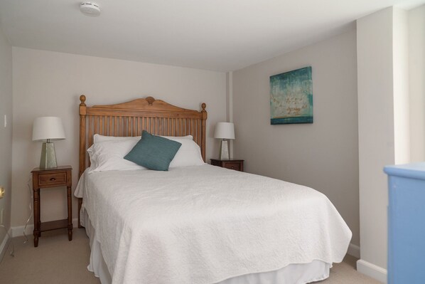 A bedroom with a wooden bed, white bedding, two bedside tables with lamps, and a painting on the wall. - Rare! Private Beachfront House in Madison CT - Sleeps 8 - Last Min Availability (Madison)