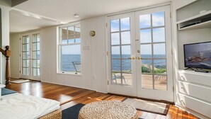 A spacious room with a large sliding glass door leading to a balcony with ocean views, wooden flooring, and a television on the right wall. - Rare! Private Beachfront House in Madison CT - Sleeps 8 - Last Min Availability (Madison)