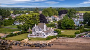 A coastal house with a large deck, a flag, and a view of the beach and surrounding houses. - Rare! Private Beachfront House in Madison CT - Sleeps 8 - Last Min Availability (Madison)