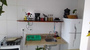 A compact kitchen with a gas stove, a sink, and a refrigerator. There are shelves above the sink holding various kitchen items.