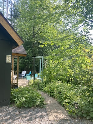 Relax in the serene garden, surrounded by lush greenery and a wooden pergola, with Adirondack chairs and a fire pit.