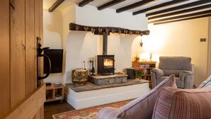 A cozy living room with a wood-burning stove, a comfortable sofa, and a television mounted on the wall. - Ingleton 2-bed Cottage, Sleeps 4, Pet Ok & Parking (Carnforth)