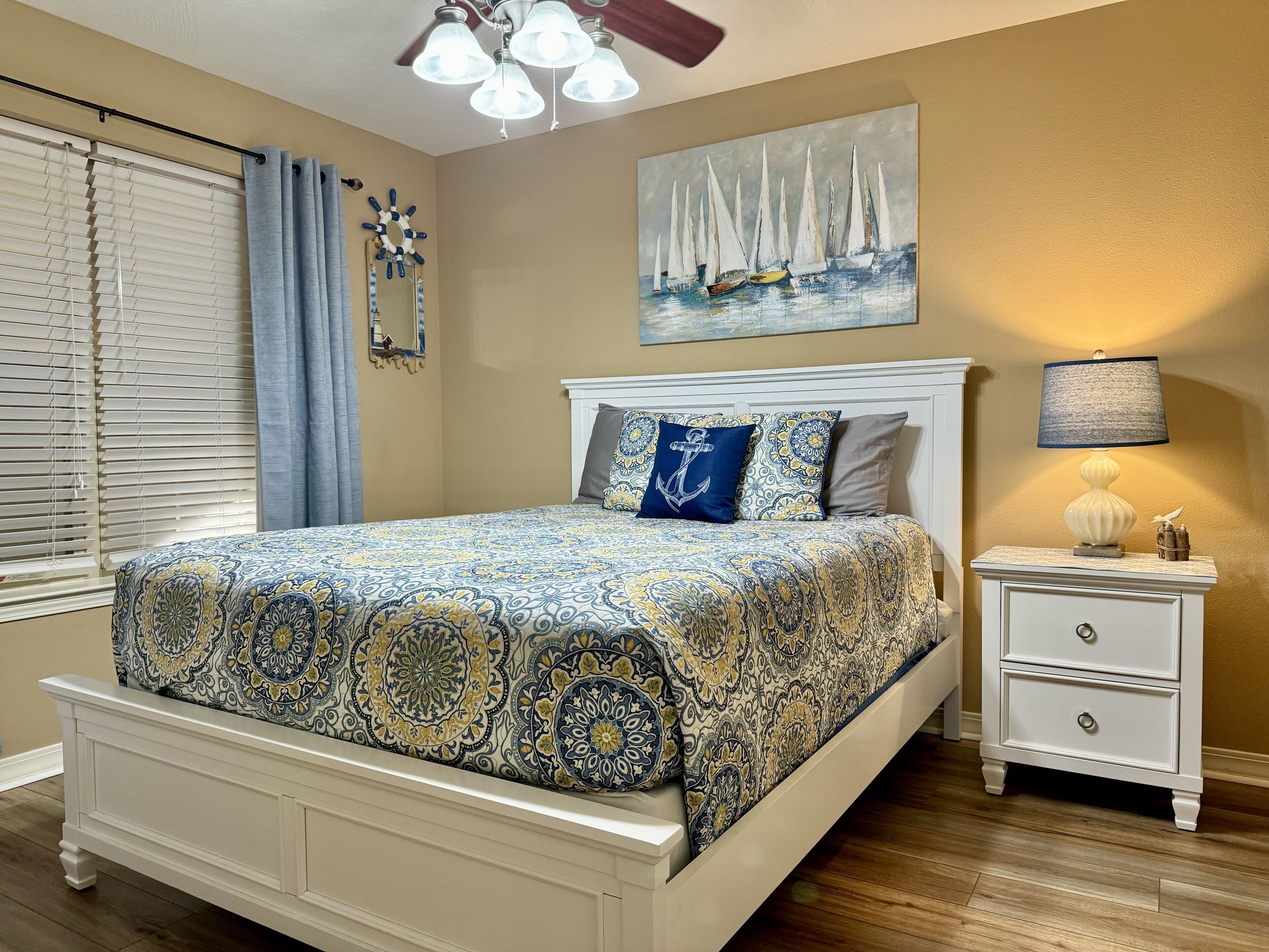 A bedroom with a bed, a nightstand, a lamp, a painting, and a window with blinds.