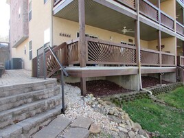 A multi-story building with a covered outdoor area, stone steps, and a wooden railing.