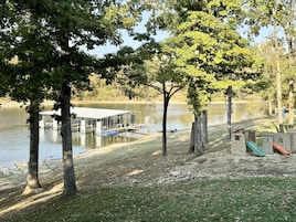 Un parque junto al lago con un muelle, un área de juegos y árboles.
