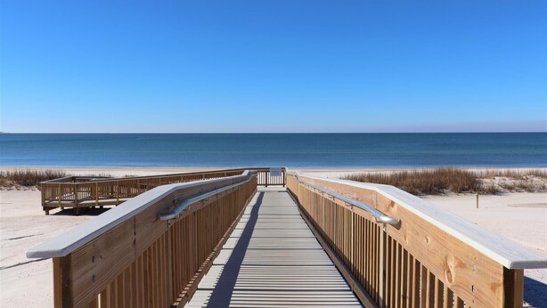 En træpromenade der fører til en strand med klare himmel.